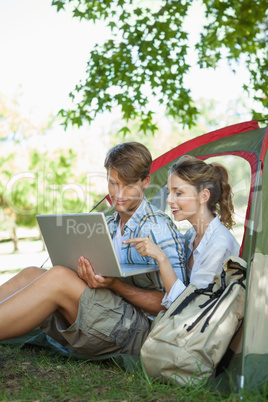 Cute couple sitting in their tent looking at laptop