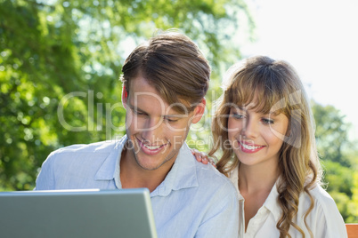 Cute couple sitting on park bench together looking at laptop