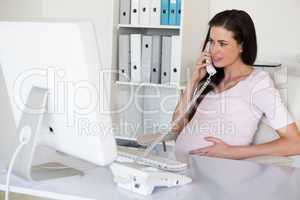 Casual pregnant businesswoman touching her bump at her desk talk