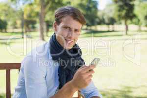 Stylish young man sitting on park bench sending a text