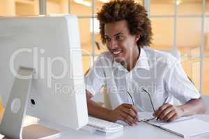 Casual young businessman sitting at his desk smiling at computer