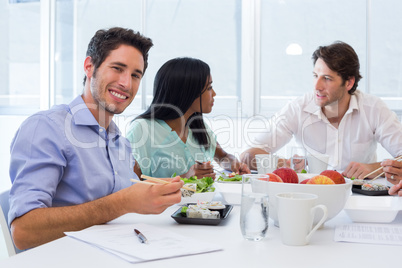 Workers chat and smile to camera while enjoying lunch