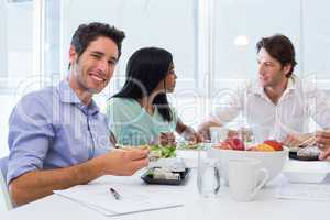 Workers chat and smile to camera while enjoying lunch