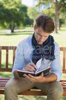 Stylish young man writing in his notepad on park bench