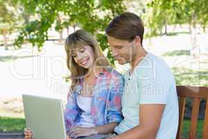 Cute young couple sitting on park bench using laptop