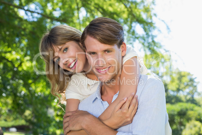 Man giving his pretty girlfriend a piggy back in the park smilin