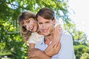 Man giving his pretty girlfriend a piggy back in the park smilin