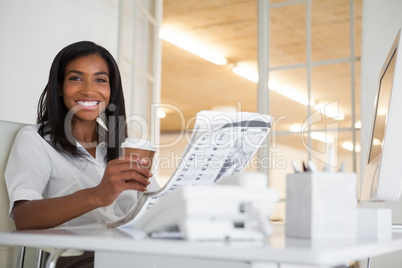 Pretty businesswoman reading newspaper at her desk