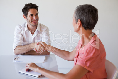 Casual business people shaking hands at desk and smiling