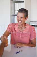 Laughing businesswoman shaking hands at desk