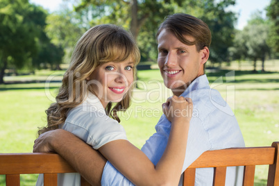 Couple relaxing on park bench together smiling at camera