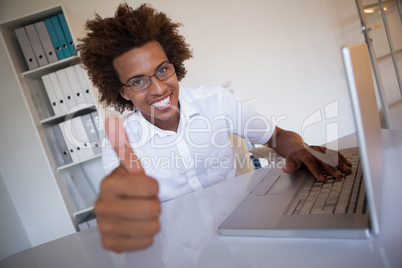 Casual businessman smiling at camera at his desk showing thumbs