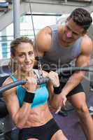 Female bodybuilder using weight machine for arms with encouragin