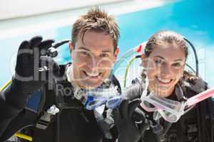 Smiling couple on scuba training in swimming pool showing ok ges