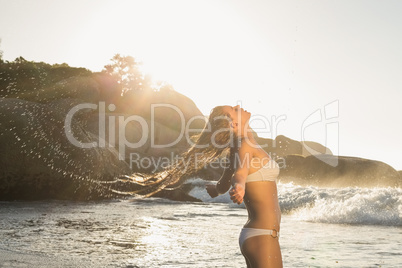 Beautiful blonde in white bikini at the beach tossing wet hair