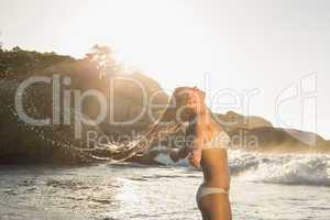 Beautiful blonde in white bikini at the beach tossing wet hair