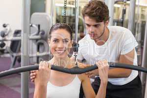 Fit brunette using weights machine for arms with trainer helping