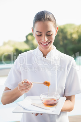 Smiling beauty therapist holding plate with honey