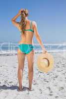 Rear view of fit woman in bikini on beach holding sunhat