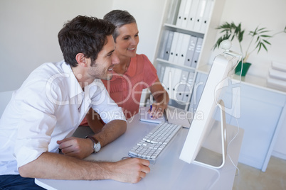 Casual business team working together at desk using computer