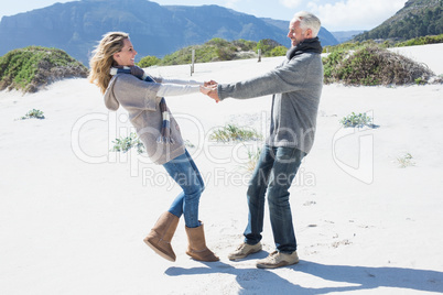 Smiling couple spinning on the beach in warm clothing