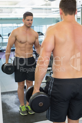 Shirtless bodybuilder lifting heavy black dumbbell looking in mi