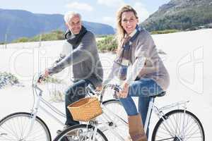 Carefree couple going on a bike ride on the beach smiling at cam