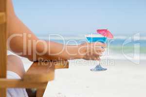 Woman sitting in deck chair with a cocktail at the beach