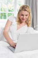 Pretty blonde lying on bed using laptop