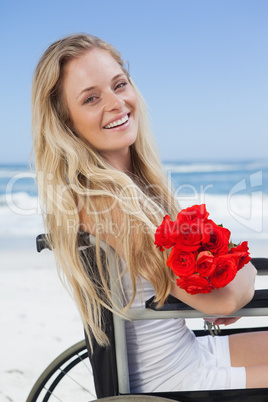 Wheelchair bound blonde smiling at the camera on the beach holdi