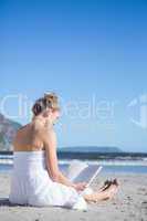 Content blonde in white dress sitting on the beach reading book