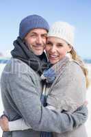 Attractive couple smiling at camera on the beach in warm clothin