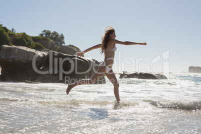 Beautiful smiling woman in white bikini leaping on the beach