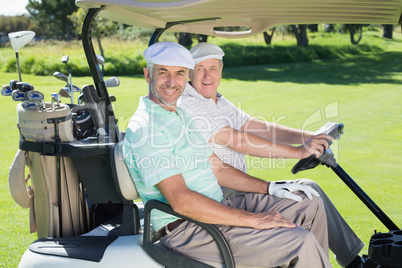 Golfing friends smiling at camera in their golf buggy