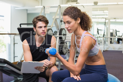 Trainer watching client lift dumbbells on exercise ball