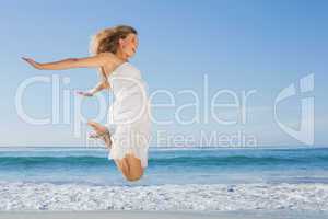 Beautiful blonde in white sundress jumping up on the beach