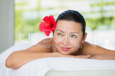 Smiling brunette lying on massage table with red lily in her hai