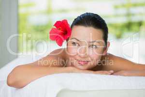 Smiling brunette lying on massage table with red lily in her hai