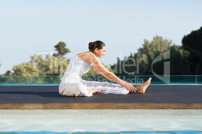Peaceful brunette in janu sirsasana yoga pose poolside