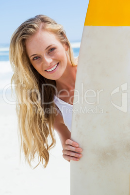 Blonde surfer holding her board smiling at camera