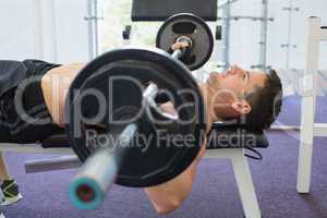 Shirtless bodybuilder lifting heavy barbell weight lying on benc
