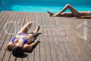 Women in bikinis lying poolside sunbathing