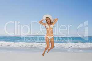 Fit smiling woman in white bikini leaping on beach