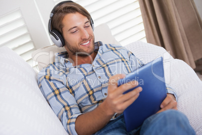 Handsome man lying on couch listening to music on tablet pc