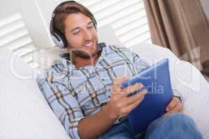 Handsome man lying on couch listening to music on tablet pc