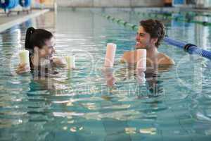 Man and woman standing with foam rollers in the pool