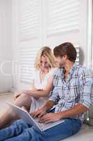 Young couple sitting on floor using laptop