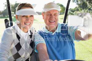 Happy golfing couple sitting in golf buggy taking a selfie