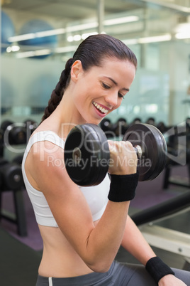 Fit smiling brunette lifting heavy black dumbbell