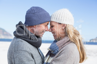 Attractive couple smiling at each other on the beach in warm clo